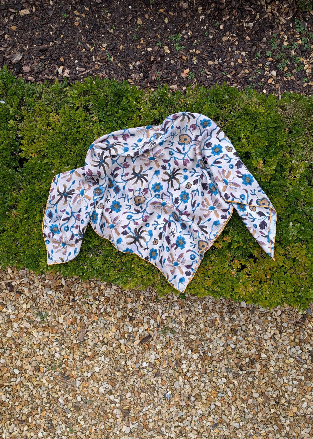 Floral-patterned silk foulard on a patch of grass next to a concrete surface