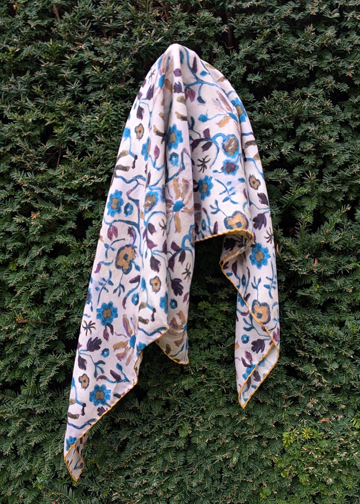 Floral-patterned silk foulard draped over a green bush