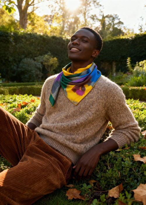 Person sitting in a garden wearing a colorful silk scarf and brown sweater