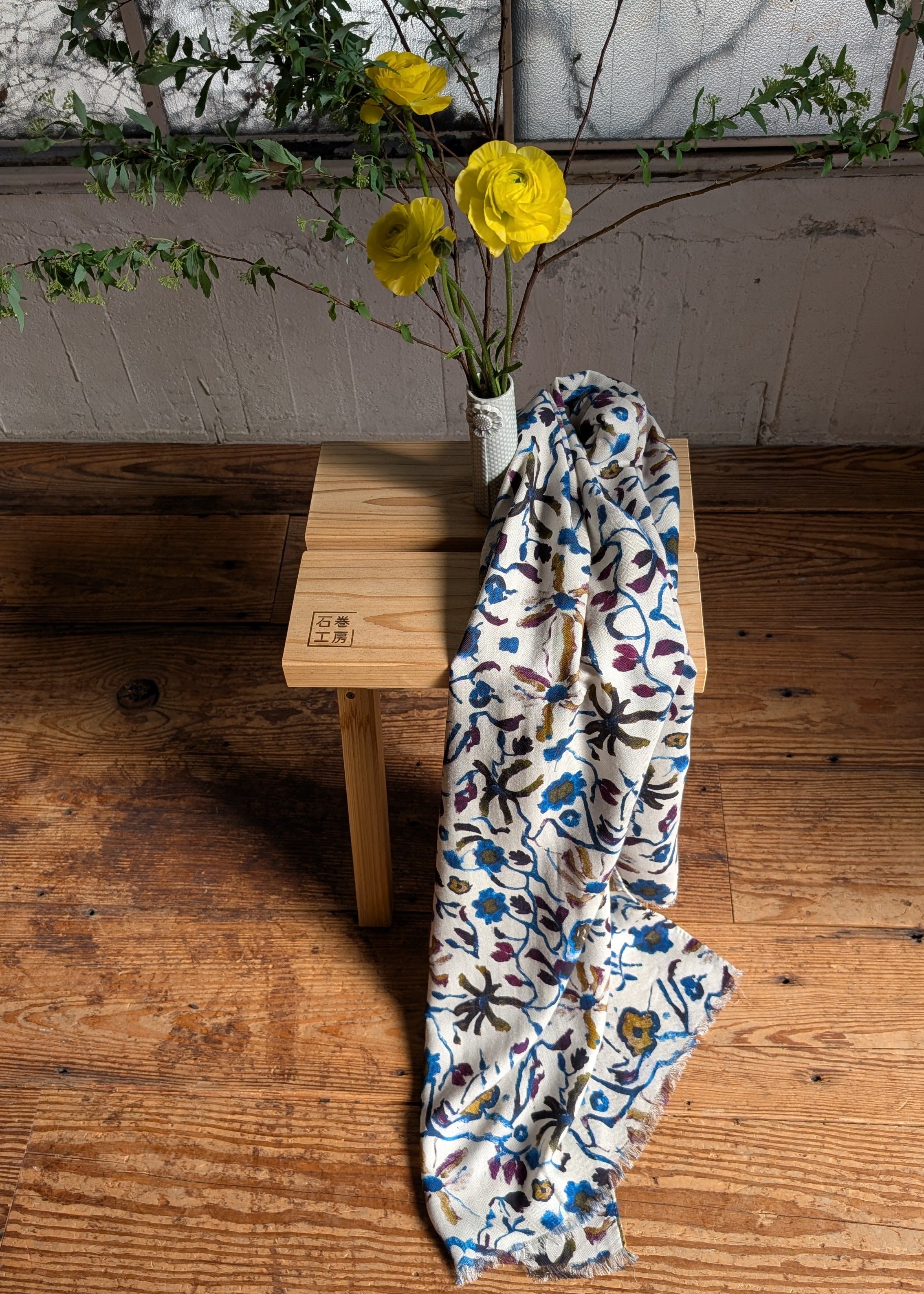 Floral-patterned wool scarf on a wooden surface with yellow flowers in the background