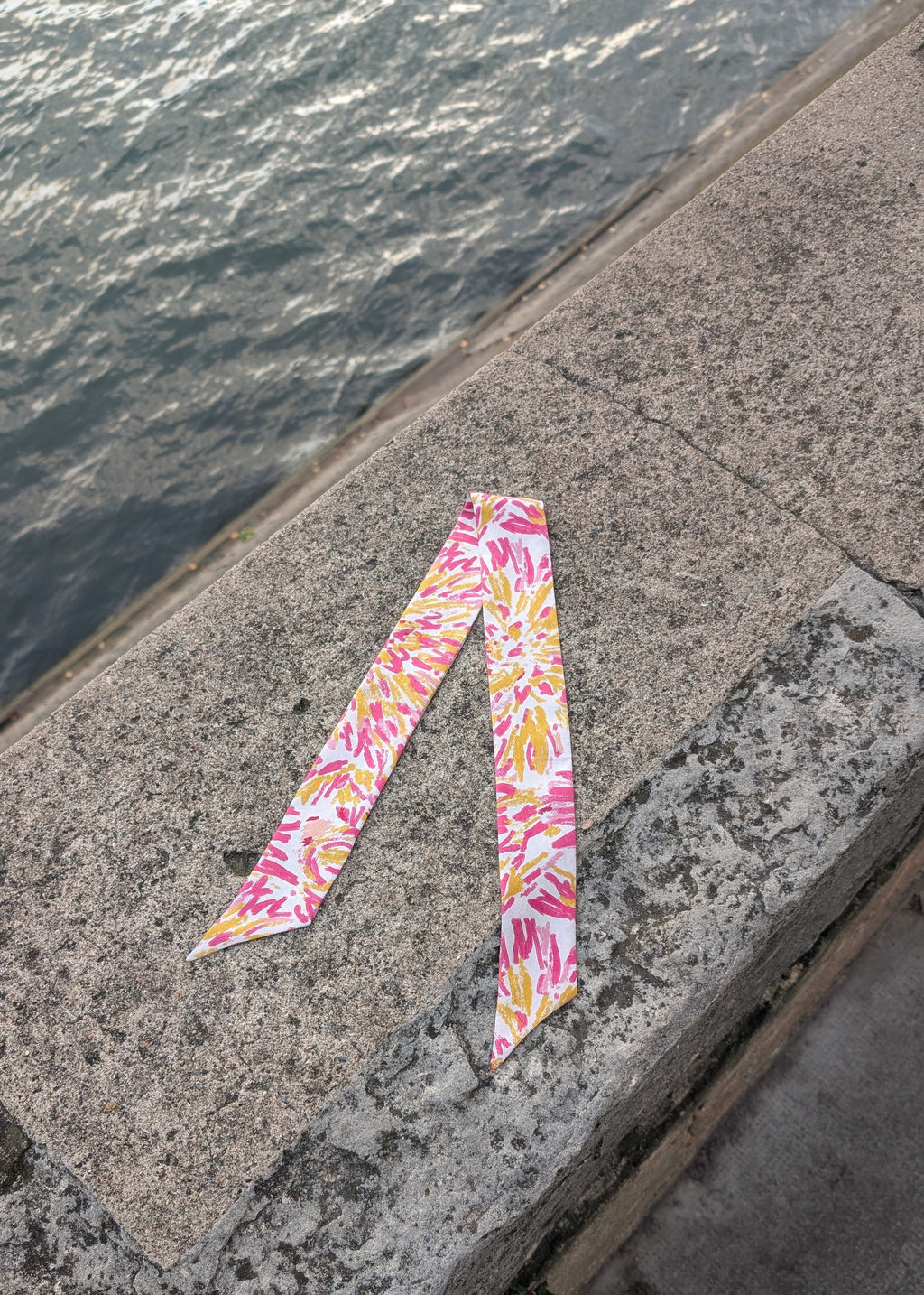 Colorful patterned silk ribbon on a concrete surface near water