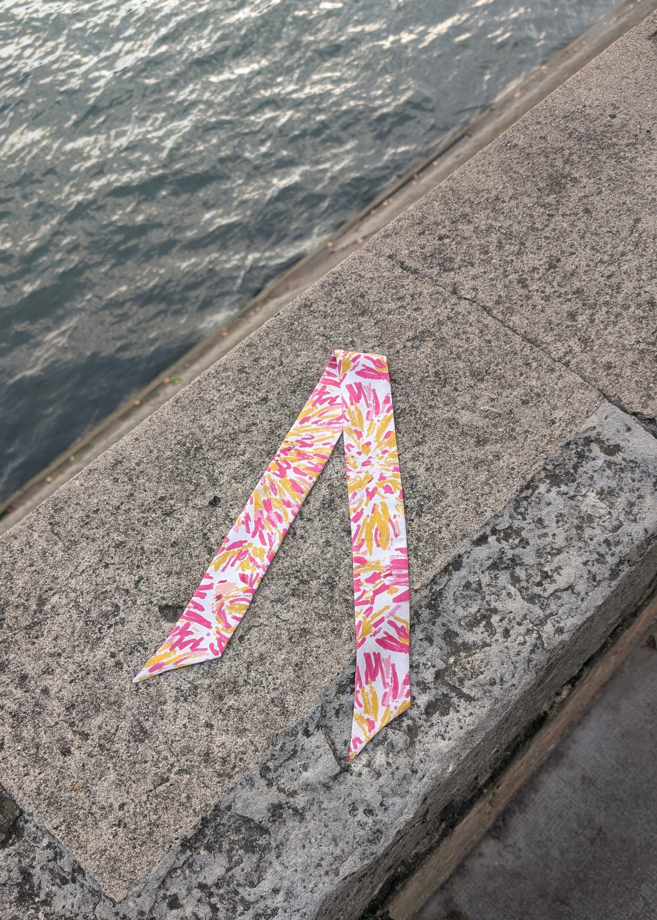 Colorful patterned silk ribbon on a concrete surface near water