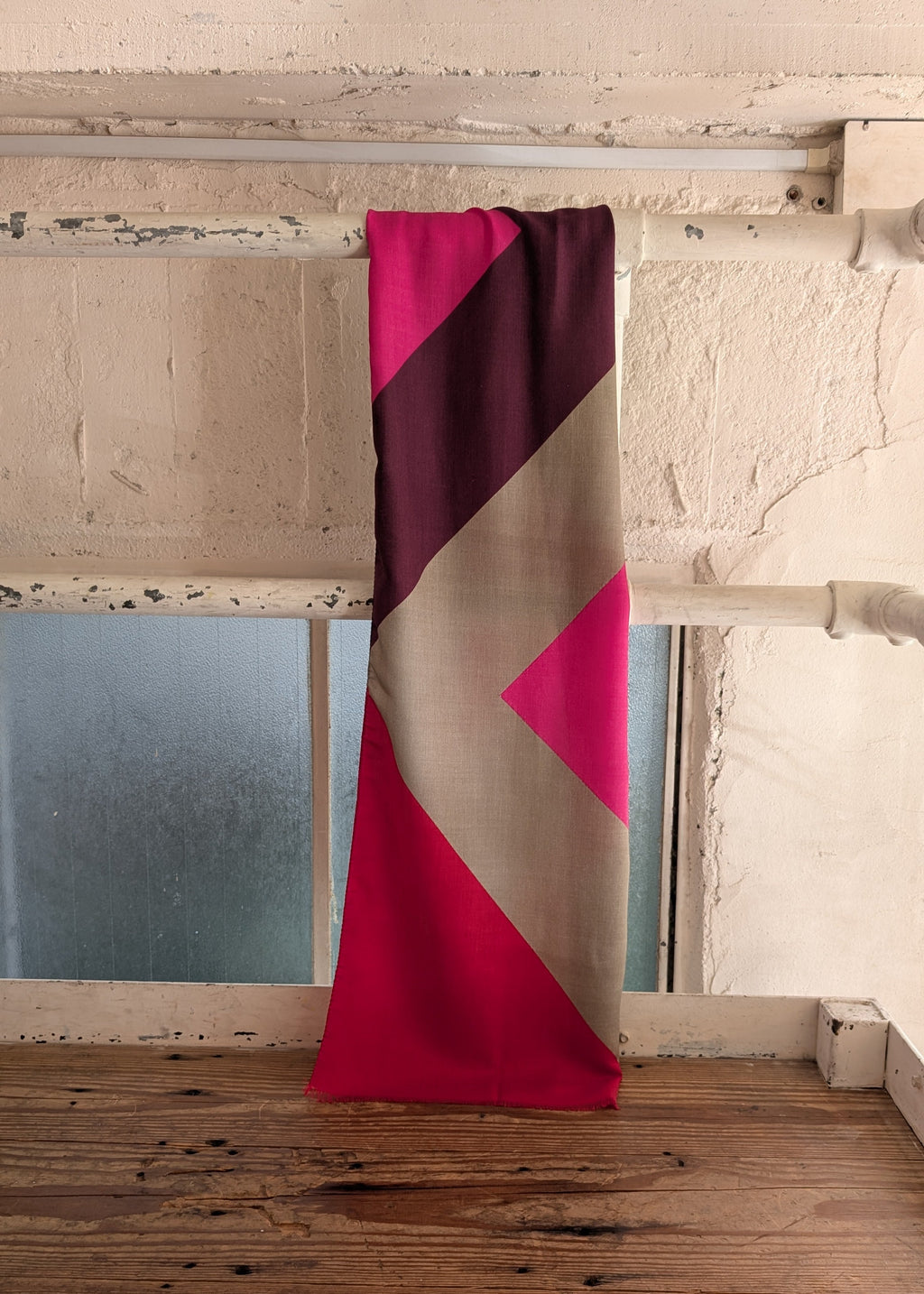 fuksia, redand  pink scarf  draped over a wooden surface with a neutral wall background